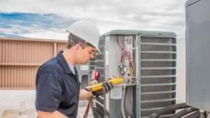 Technician in safety gear inspecting an air conditioning capacitor with a multimeter tool outdoors.