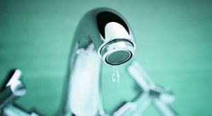 Close-up of a chrome faucet aerator with water droplets against a green background, highlighting water conservation and plumbing fixtures.
