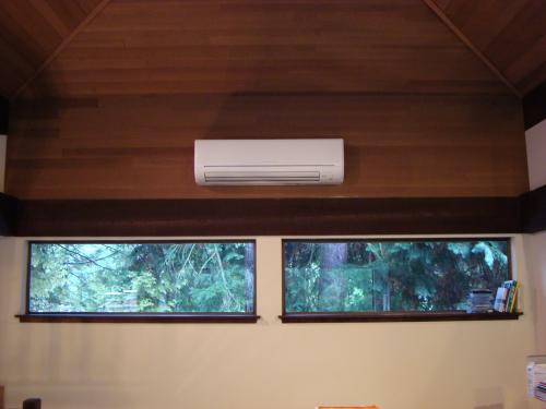 Interior office room featuring wooden ceiling with mounted white split-system air conditioner and two horizontal aquarium windows in beige walls.